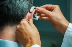 Audiologist fitting hearing aid on an older man